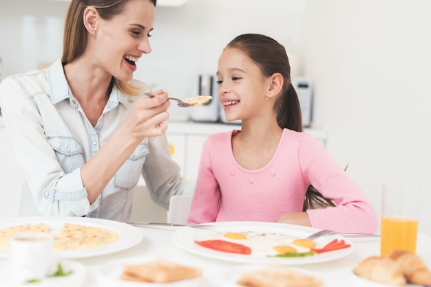 Mãe e filha estão sentados na cozinha e comendo.