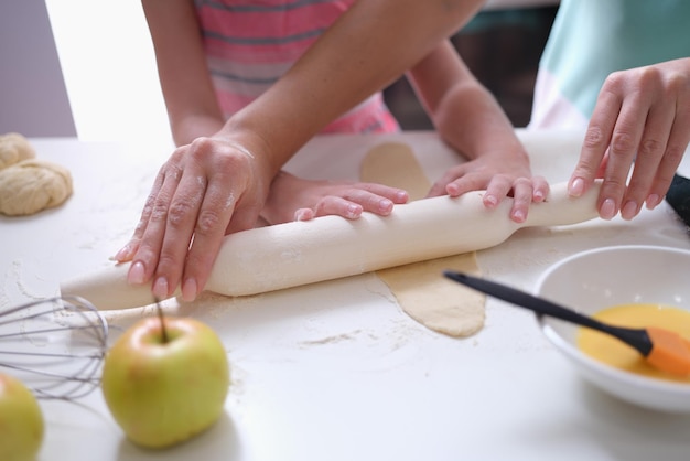 Mãe e filha estendem a massa com rolo na cozinha