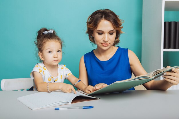 Mãe e filha estudando em casa à mesa.