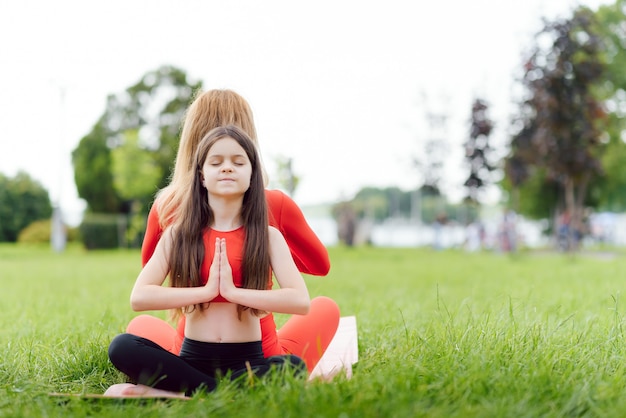 Mãe e filha fazendo exercícios de ioga na grama do parque durante o dia