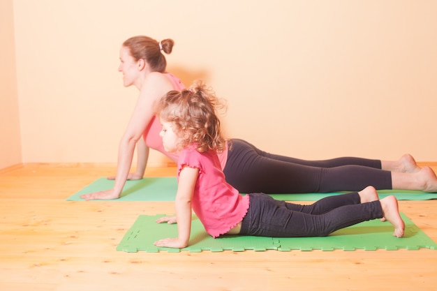 Mãe e filha fazendo exercícios de ioga no tapete verde