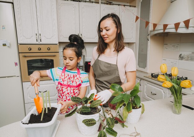 Mãe e filha fazendo transplante de primavera e regando plantas e flores em casa