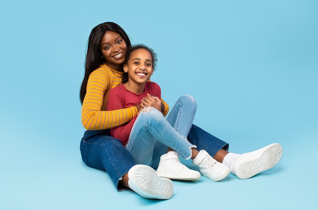 Mãe e filha Feliz mãe negra e criança se unindo enquanto estão sentadas no chão sobre fundo azul