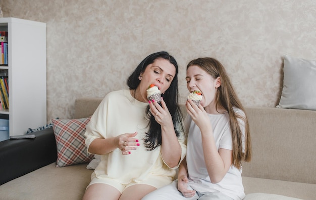 Mãe e filha felizes comendo um delicioso bolo de morango sentadas em casa no sofá