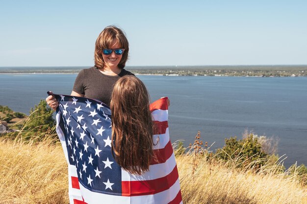 Mãe e filha felizes da família com bandeira americana apreciam a natureza