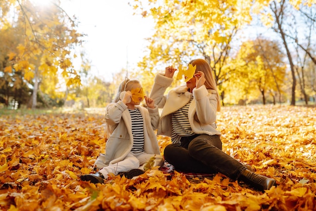 Mãe e filha felizes se divertem no parque de outono ao pôr do sol Família em caminhada Caminhadas de infância descansam