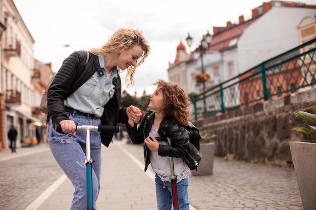 Mãe e filha idênticas com scooters na cidade