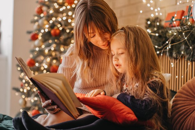 Mãe e filha lendo contos de fadas na véspera de Natal, atmosfera maravilhosa de amor e confiança, crença em milagres, boas festas