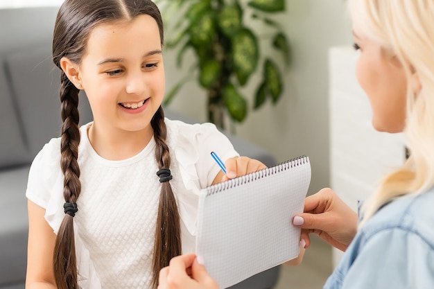 Mãe e filha linda e feliz fazem um cartão para o dia das mães sentados juntos à mesa com papel e lápis.