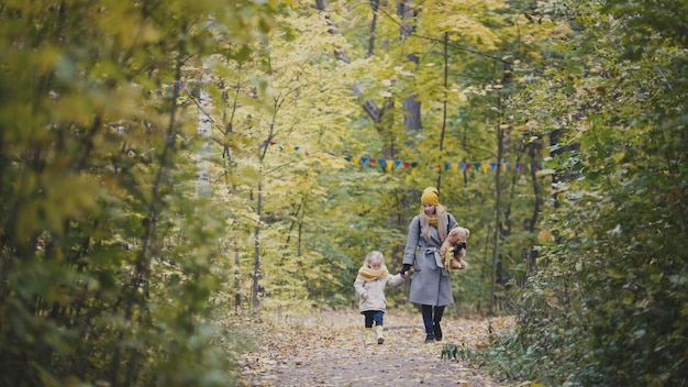 Mãe e filha, menina, caminhando em um parque de outono, criança e ursinho de pelúcia, telefoto