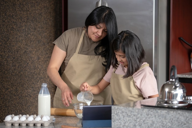 Mãe e filha mexicana cozinhando na cozinha olhando a receita em um tablet