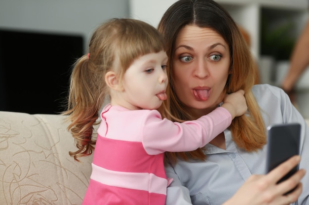 Mãe e filha mostram línguas na câmera se divertindo tirando selfie no smartphone