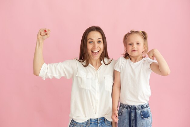 Foto mãe e filha mostram seus músculos e força no estúdio em um fundo rosa.