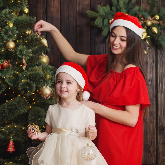 Mãe e filha na árvore de natal em uma madeira escura