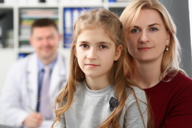 Mãe e filha na consulta médica sorriem para trás