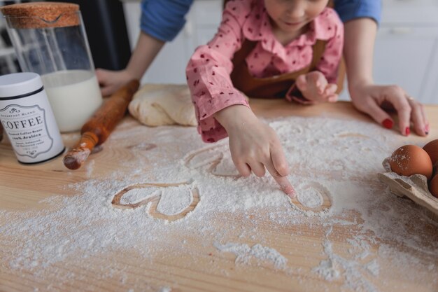 mãe e filha na cozinha preparam comida com farinha e desenham corações na farinha