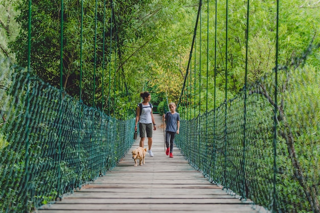 Mãe e filha na floresta andando sobre a ponte de madeira