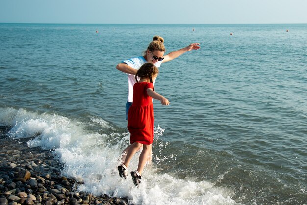 Mãe e filha na praia pulam nas ondas e se divertem. Período de férias. Férias em família.