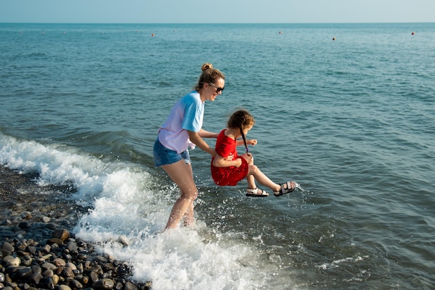 Mãe e filha na praia pulam nas ondas e se divertem. Período de férias.