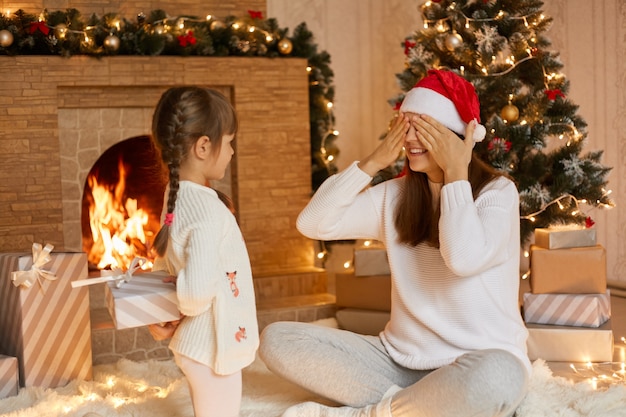 Mãe e filha na sala de estar, menina dando um presente para a mãe na véspera de natal