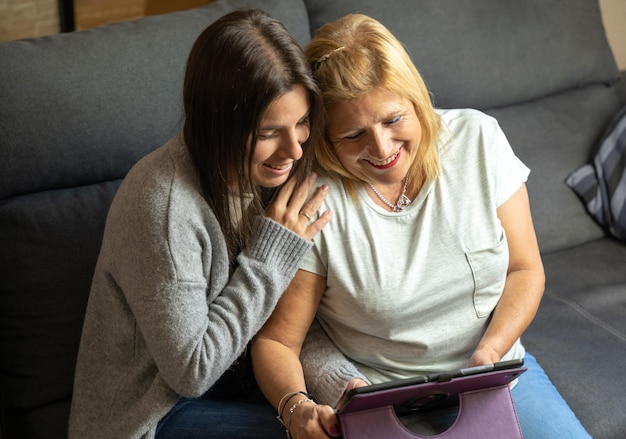Mãe e filha no sofá em casa enquanto olham para o tablet e são felizes