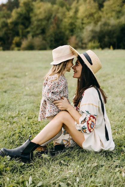 Foto mãe e filha pequena brincando de nariz a nariz e sorrindo, ambas vestindo chapéus de palha.