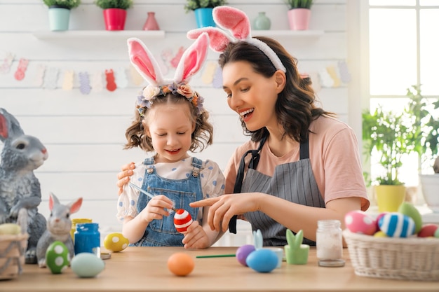 Mãe e filha pintando ovos. Família feliz se preparando para a Páscoa. Criança menina bonitinha usando orelhas de coelho.