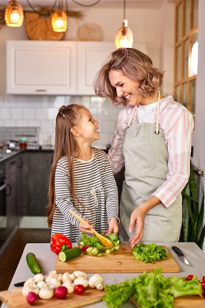 Mãe e filha preparando comida saudável para a família, salada vegana feita de vegetais frescos, misture