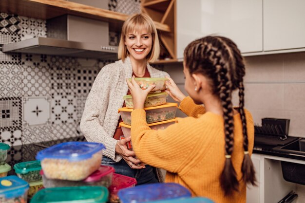 Mãe e filha preparando legumes para o inverno em recipientes a vácuo.