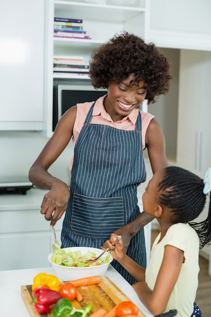 Mãe e filha preparando salada na cozinha em casa