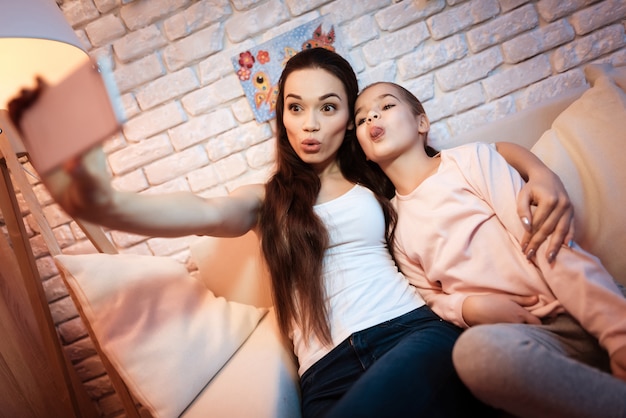 Mãe e filha que tomam o selfie no telefone na noite em casa.