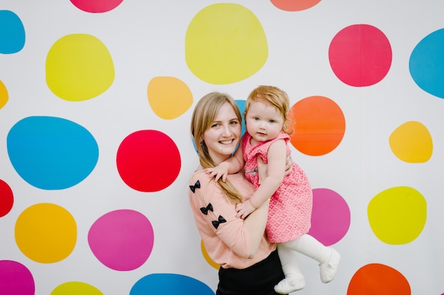 Foto mãe e filha rindo e felizes estão de pé sobre um fundo colorido. conceito de alegria. família feliz, meninas perto de um fundo colorido.