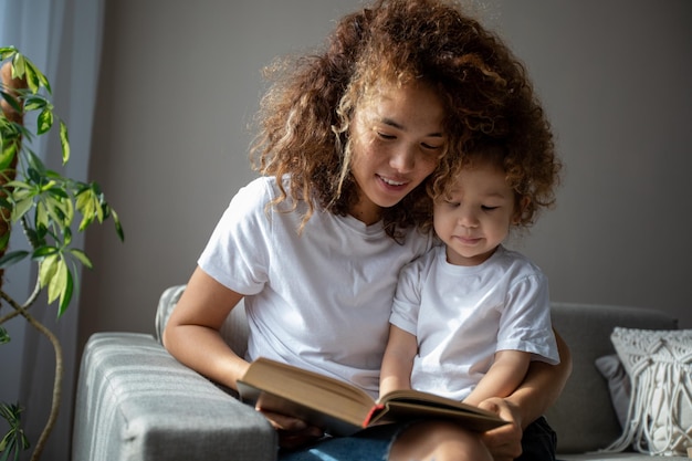 Mãe e filha rizadas em camisas brancas lendo um livro