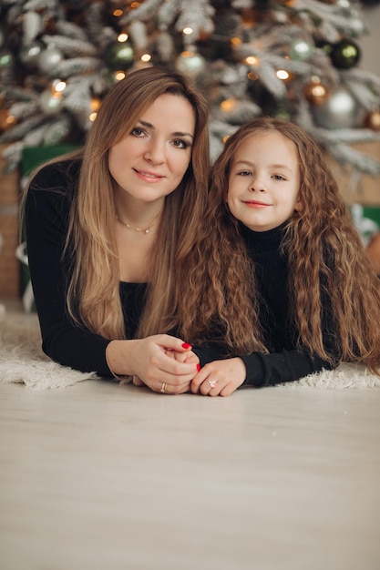 Mãe e filha se abraçam e posam no natal ao lado de uma árvore de natal e presentes uma família feliz em um quarto decorado de ano novo está se divertindo