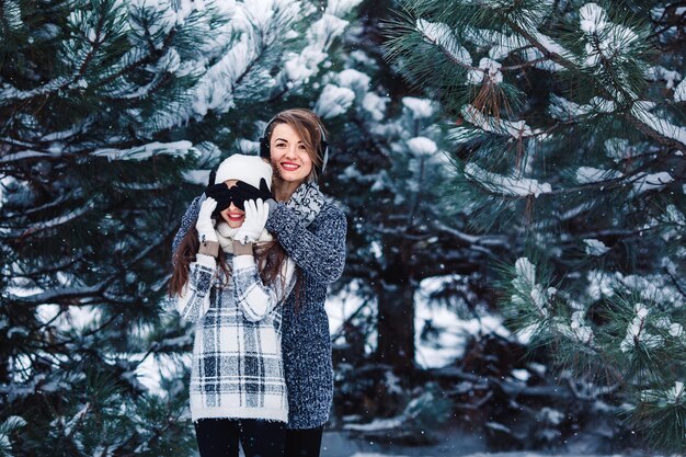 Mãe e filha se divertem brincando na floresta de inverno