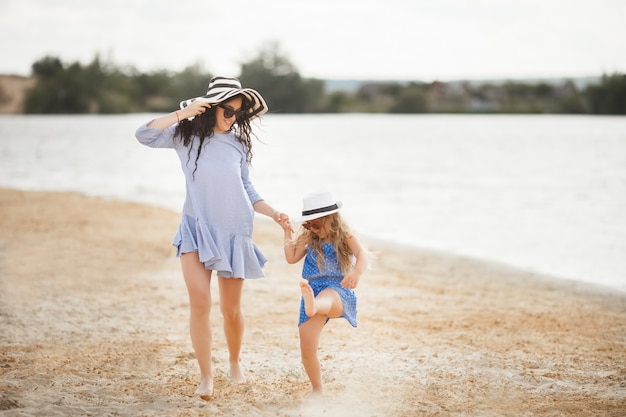 Mãe e filha se divertindo no litoral. Jovem mãe bonita e seu filho brincando perto da água