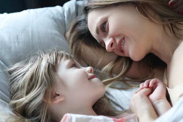 Mãe e filha se olhando e deitadas na cama