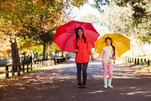 Mãe e filha segurando guarda-chuvas na rua no parque