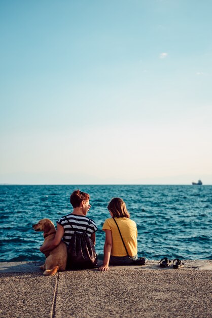 Mãe e filha sentada à beira-mar com cachorro