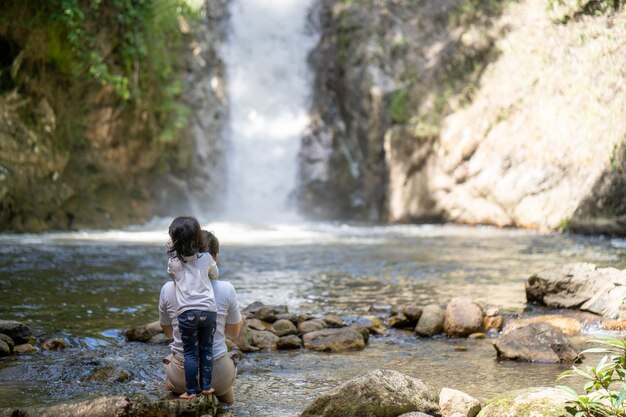 Mãe e filha sentada nas rochas contra a cachoeira na floresta da floresta.