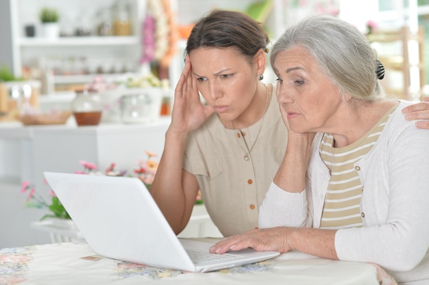 Mãe e filha sentadas à mesa com laptop em casa