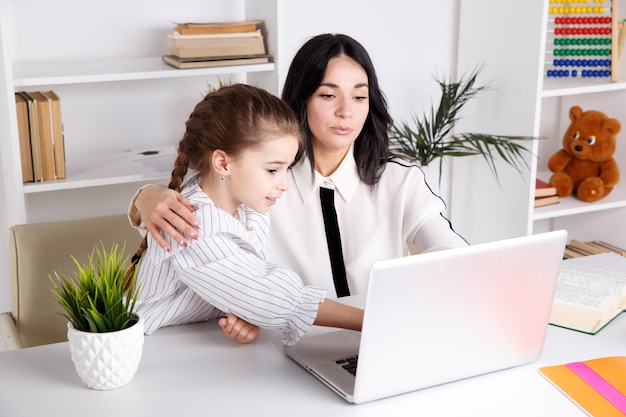 Mãe e filha sentadas juntas com o computador na mesa.