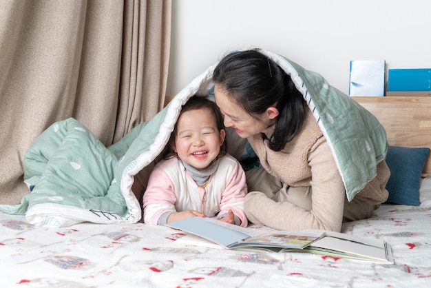 Mãe e filha sentadas na cama lendo juntas