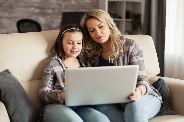 Mãe e filha sentadas no sofá da sala assistindo a um filme no laptop.