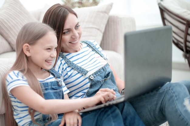 Mãe e filha sentadas no tapete da sala e usando um laptop