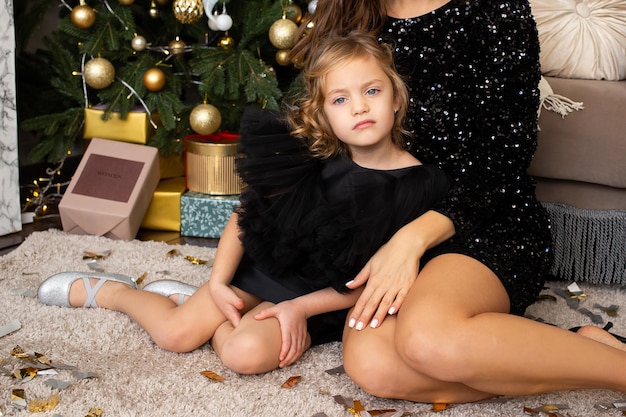 Mãe e filha sentadas perto da árvore de Natal em casa Feliz Natal e Boas Festas