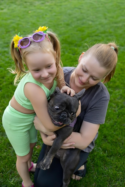 Foto mãe e filha sentam no gramado do parque e abraçam o cachorro