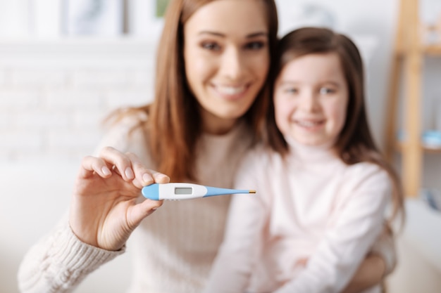 Mãe e filha sorrindo positivamente segurando o termômetro e expressando alegria após a recuperação