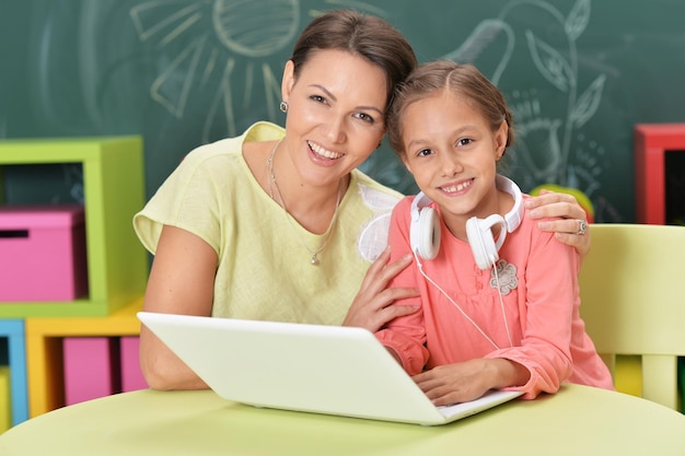 Mãe e filha usando laptop com quadro-negro no fundo