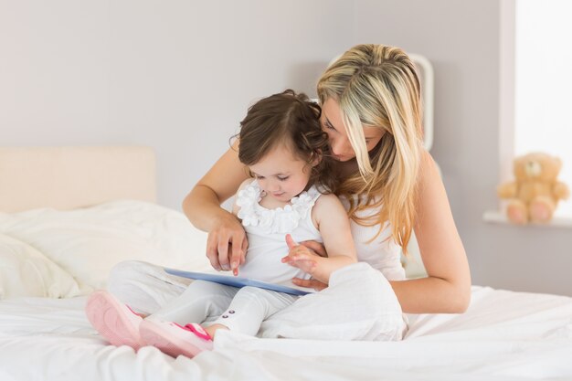 Mãe e filha usando o tablet digital na cama